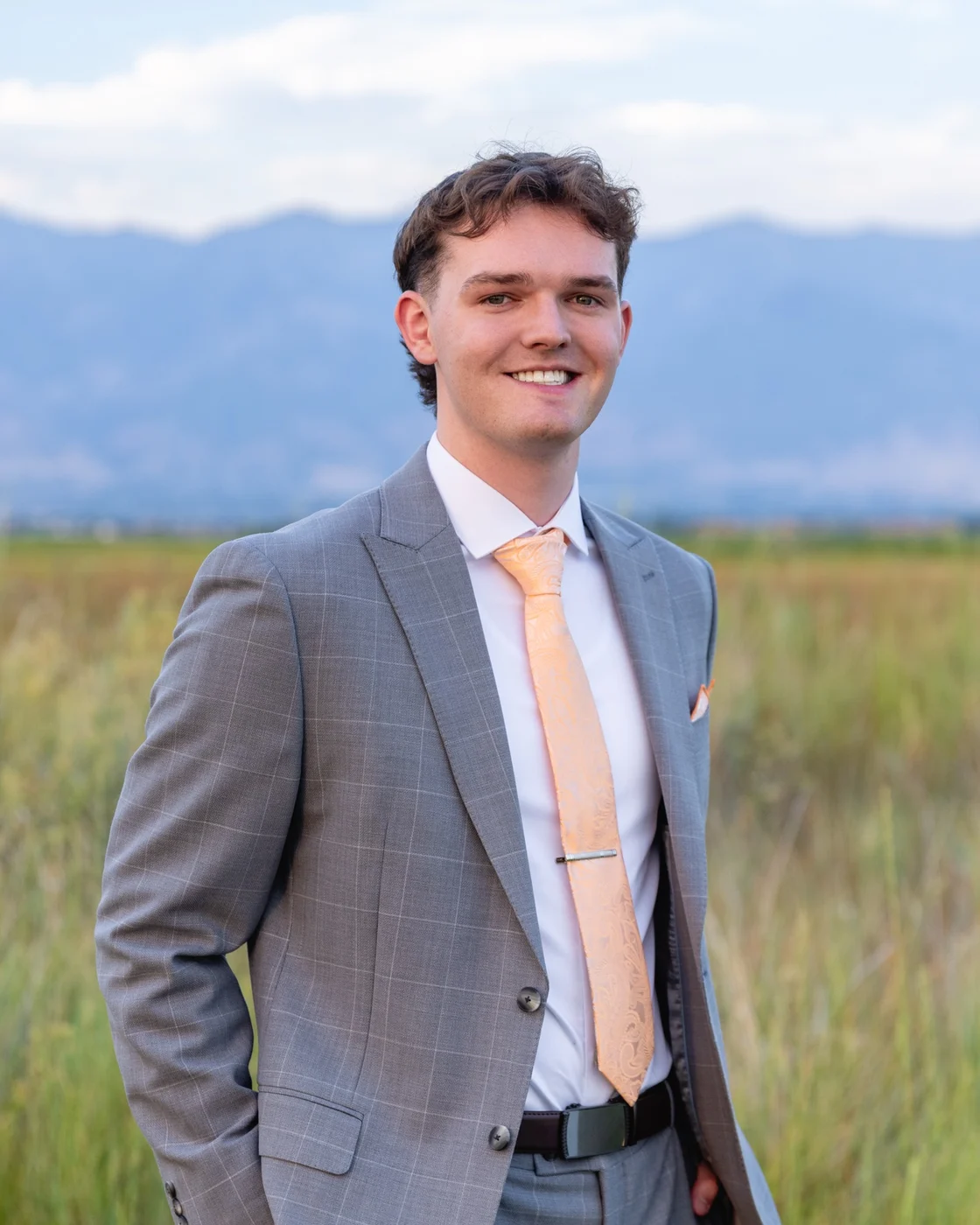 Rylek Staker in a grey suit, standing in a field below the Wasatch mountains
